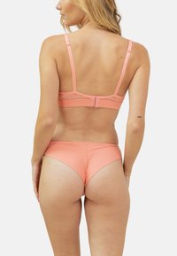 Ensemble de lingerie rose comprenant un bralette à bretelles ajustables et finition en dentelle, associé à un bikini taille basse assorti, mettant en valeur une texture de tissu lisse.