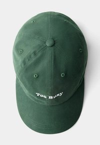 Casquette de baseball en coton vert avec une visière courbée et le texte brodé "Trop Occupé" en blanc à l'avant. Tissu texturé avec des trous de ventilation.