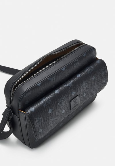 Zwarte leren tas met gestructureerd oppervlak, dubbele ritscompartimenten, een zak met klep aan de voorkant en logo-accenten. Gladde afwerking met contrasterende voering.