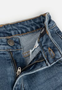 Niebieskie dżinsy o teksturowanym wykończeniu. Posiadają srebrny zamek, zapięcie na guzik oraz widoczne detale przeszyć. Wewnętrzna podszewka jest jasnoniebieska.