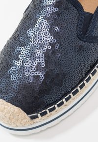 Espadrille marine avec une tige en sequins, dotée d'une semelle en jute tissée, de coutures blanches contrastantes et d'une finition texturée pour plus de détails.
