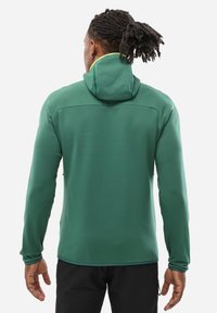 Green hooded jacket made of smooth fabric, featuring a contrast yellow lining along the hood and seams, with long sleeves and a relaxed fit.