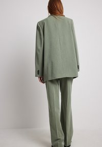 Ljusgrön kostymuppsättning gjord av strukturerad tyg, med en löst sittande blazer med rak skärning och vida byxor. Bakifrån visad.