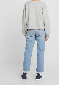 Graues, kurz geschnittenes Sweatshirt mit lockerem Sitz, kombiniert mit hellblauen Jeans mit geradem Bein und ausgefranstem Saum sowie blauen Turnschuhen.