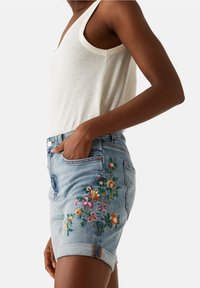Shorts in denim con un lavaggio azzurro chiaro, con ricami floreali colorati sul lato sinistro e orlo arrotolato. Materiale in misto cotone.