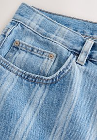 Hele sinine teksariie, millel on tekstuuriga pind vertikaalse pleekimisega, väike tagatasku metallnööpnõeltega ja kontrastõmblused.