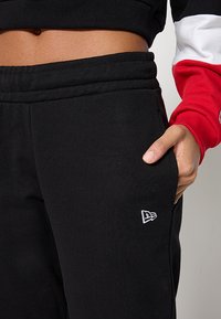 Černé tepláky z jemného úpletu s elastickým pasem, s malým bílým logem na levé kapse a standardním střihem.