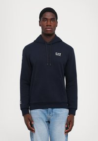 Felpa con cappuccio blu navy in tessuto morbido, dotata di tasca a marsupio, coulisse regolabile e dettagli con logo sul petto e sulla manica.