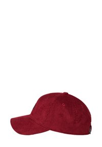 Punainen corduroy-baseball-lippis, jossa on tekstuuri pinta, ommeltu yksityiskohtia ja kaareva lippa. Varustettu ilmanvaihtoaukoilla ja bränditagilla sivulla.
