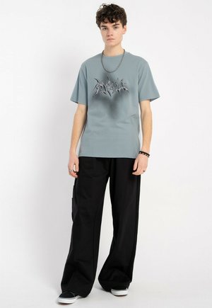 Koszulka z krótkim rękawem w jasnoniebieskim kolorze z graficznym wzorem na przedzie, połączona z luźnymi czarnymi spodniami i czarnymi sneakersami.