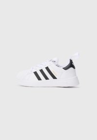 Λευκό αθλητικό παπούτσι Adidas Superstar με μαύρες ρίγες, χρυσή επιγραφή "Superstar", μαύρη γλώσσα στη φτέρνα και λευκή θηλιά τραβήγματος, πλευρική όψη σε απλό φόντο.