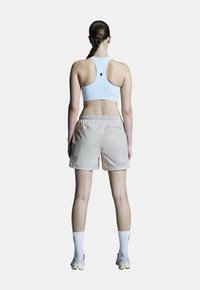Hellblauer Sport-BH mit Racerback-Design, kombiniert mit beigen Shorts mit elastischem Bund; weiße Socken und helle Sneaker runden das Outfit ab.