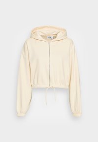 Felpa corta di colore crema realizzata in tessuto morbido, con zip frontale, vita con cordino e polsini elasticizzati, oltre a un ampio cappuccio.