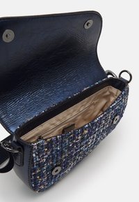 Sac à main en tissu tissé texturé multicolore en navy, avec un intérieur en cuir lisse. Équipé d'une fermeture à aimant et d'accents en métal argenté.