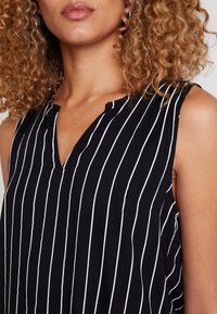 Svart och vit randig ärmlös topp med V-ringning, mjuk textur och sidoflikar, designad för en avslappnad passform.