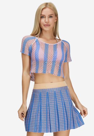 Donna che indossa un top corto lavorato a uncinetto a righe rosa e blu e una gonna plissettata a quadri blu e beige.