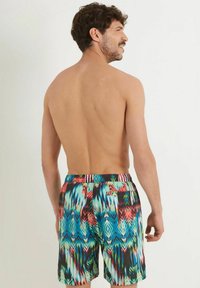 Costumi da bagno colorati con un motivo vivace caratterizzato da forme astratte blu, rosse e verdi; cintura elastica; dettaglio della tasca sul retro.
