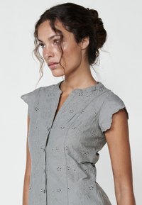 Graues gesticktes Kleid mit floralem Muster, kurzen Puffärmeln, Kragen und Knopfleiste. Textil mit strukturiertem Stoff und filigranen Details.
