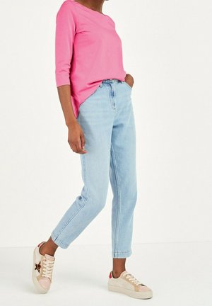 Person trägt ein pinkes Dreiviertelarm-Oberteil, hellblaue hoch taillierte Jeans und beige Sneaker mit Leopardenmuster-Sternakzenten.