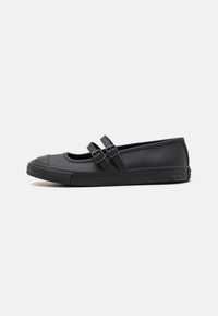 Sapatos pretos de sola plana com bico redondo, duas tiras cruzadas sobre o peito do pé, textura suave e solado de borracha com padrão texturizado.