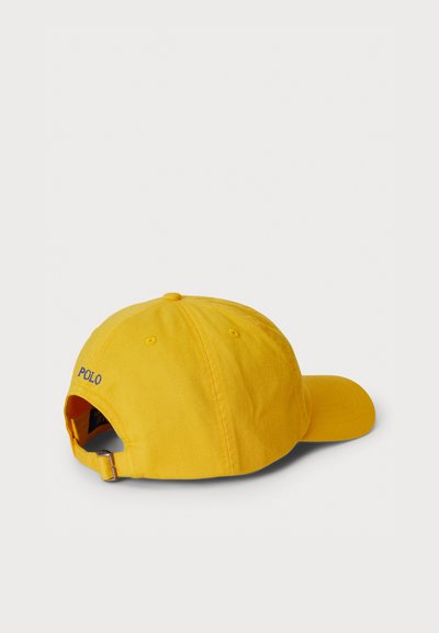 Κίτρινο βαμβακερό καπέλο με κυρτή γείσο, ρυθμιζόμενο πίσω λουράκι και κεντημένο "POLO" με μπλε χρώμα στην αριστερή πλευρά. Απλός σχεδιασμός, ανθεκτικό υλικό.