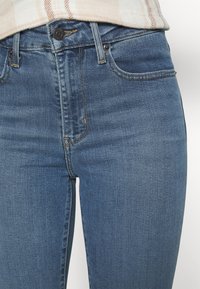 Jeans de tiro alto en azul, fabricados en denim, con un diseño clásico de cinco bolsillos, costuras sutiles y un cierre de botón en la cintura.