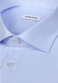 Chemise de costume bleu clair texturée avec col boutonné et étiquette de marque visible cousue à l'intérieur du col indiquant "seidensticker."