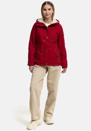 Rode hoodie met een zachte, crèmekleurige voering, ritszakken en verstelbare trekkoorden. Gecombineerd met crèmekleurige broeken en sneakers.