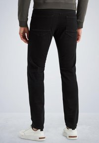 Crne slim-fit traperice s dva stražnja džepa, s blagim izbljeđenjima, uparene s bijelim cipelama koje imaju smeđi naglasak na potplatu.