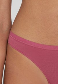 Różowe bikini dolne wykonane z gładkiego materiału. Charakteryzuje się wąskim pasem i minimalnym krojem, z estetycznym przeszyciem wzdłuż brzegów.