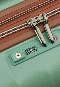 Valise rigide verte avec une fermeture éclair brune à deux tirettes métalliques. Comprend un cadenas à combinaison avec un trou de clé, marqué "Delsey."