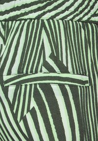 Grön tyg med svarta och ljusgröna vertikala ränder. Inkluderar en horisontell ficka med en ren, sydd kant. Mjukt, texturerat material.