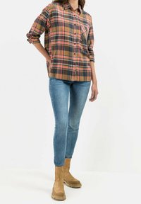 Camicia a quadri nei toni marrone, arancione e blu navy, abbinata a jeans skinny blu e stivaletti alla caviglia in suede beige con suola spessa.