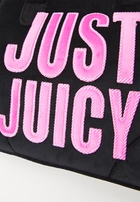 Fekete szöveten nagy, árnyékolt rózsaszín hímzett "JUST JUICY" felirat található, texturált felülettel.