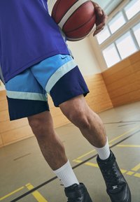 Marineblå og lyseblå trening-shorts med geometriske striper, kombinert med svarte joggesko og hvite sokker, holder en basketball.
