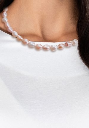 Collier avec des perles irrégulières rose pâle et blanches sur un fil, porté sur un haut en tissu blanc texturé.
