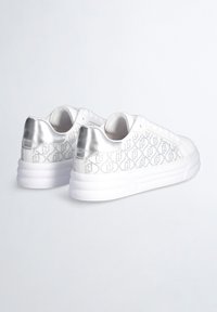 Sneakers bianchi con un accento metallico argentato sul tallone e un design tessile stampato sui lati. Suola spessa e imbottita per il comfort.