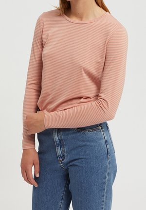 Kvinde iført en tætsiddende, lyserød langærmet top med tynde, vandrette striber, kombineret med højtaljede blå jeans.