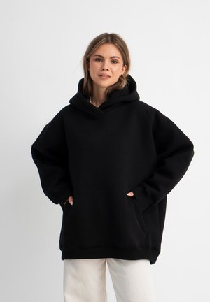 Zwarte oversized hoodie met grote voorkruiszak en geribbelde manchetten, voorzien van een trekkoordhoed en een zachte, gestructureerde stof.
