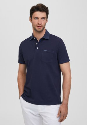 Polo de color marino hecho de algodón, con cuello, tres botones y un bolsillo en el pecho. Mangas cortas y un dobladillo recto con abertura lateral.