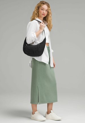 Melna auduma rokassoma ar izliekumu, sudraba rāvējslēdzējiem, valkāta uz pleca. Modelis baltā pogāmā krekliņā, zaļā midi svārkos un baltajās sporta kedās.