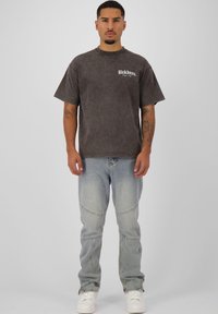 Grijze, korte mouwen t-shirt met een vervaagde afwerking, voorzien van een klein wit logo. Gecombineerd met lichtblauwe, smalle jeans en witte sneakers.