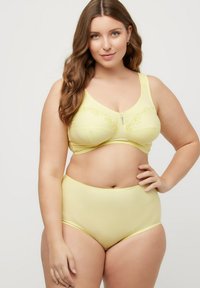 Keltainen rintaliivi ja korkeavyötäröiset alushousut ribbikankaasta, joissa on kukkakirjontaa ja pieni koristeellinen hakaset rintaliivissä.