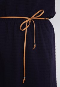 Vestido de tela azul marino con rayas texturizadas, ajustado en la cintura con un cordón color marrón claro adornado con cuentas metálicas decorativas.