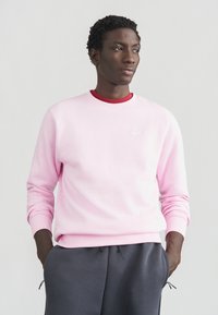 Sweatshirt cor de rosa claro com decote redondo e punhos canelados, com um pequeno logótipo branco da Nike no peito, combinado com calças cinza escuro.