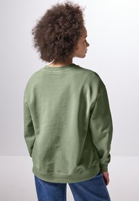 Felpa verde con maniche lunghe, colletto rotondo, polsini e orlo a coste. Vestibilità rilassata, realizzata in un tessuto morbido, esposta su uno sfondo neutro.