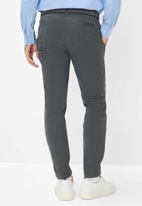 Pantalon en coton gris avec coupe slim, doté de poches arrière et d'une ceinture avec passants, associé à des baskets blanches.