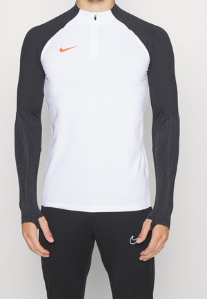 Mand iført en hvid og sort langærmet Nike sportstop med sorte bukser med et hvidt Nike swoosh-logo.