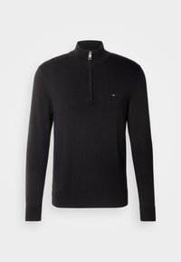 Pull-over noir à manches longues avec un col demi-fermeture éclair et un petit logo rouge, blanc et bleu sur le côté gauche de la poitrine.