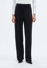 Μαύρο παντελόνι κομμένο και ραμμένο με ψηλή μέση, διαθέτει διπλές πιέτες μπροστά, λείο φινίρισμα και διακριτικές ραφές. Συνδυάζεται με μυτερά παπούτσια.